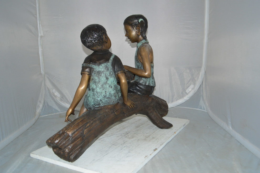Boy and Girl on a tree log reading Bronze Statue -  Size: 37"L x 14"W x 27"H.