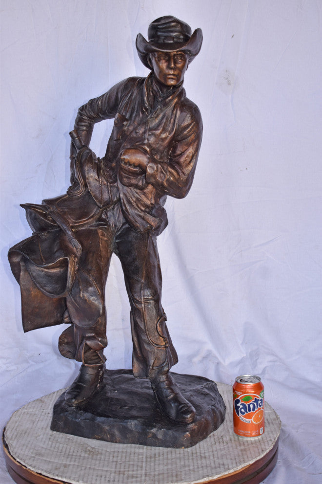 Cowboy Holding His Saddle Bronze Statue - Size: 20"L x 14"W x 35"H.